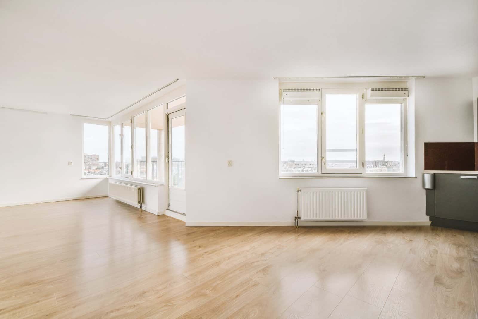 Bright empty living room with large windows and wooden flooring.