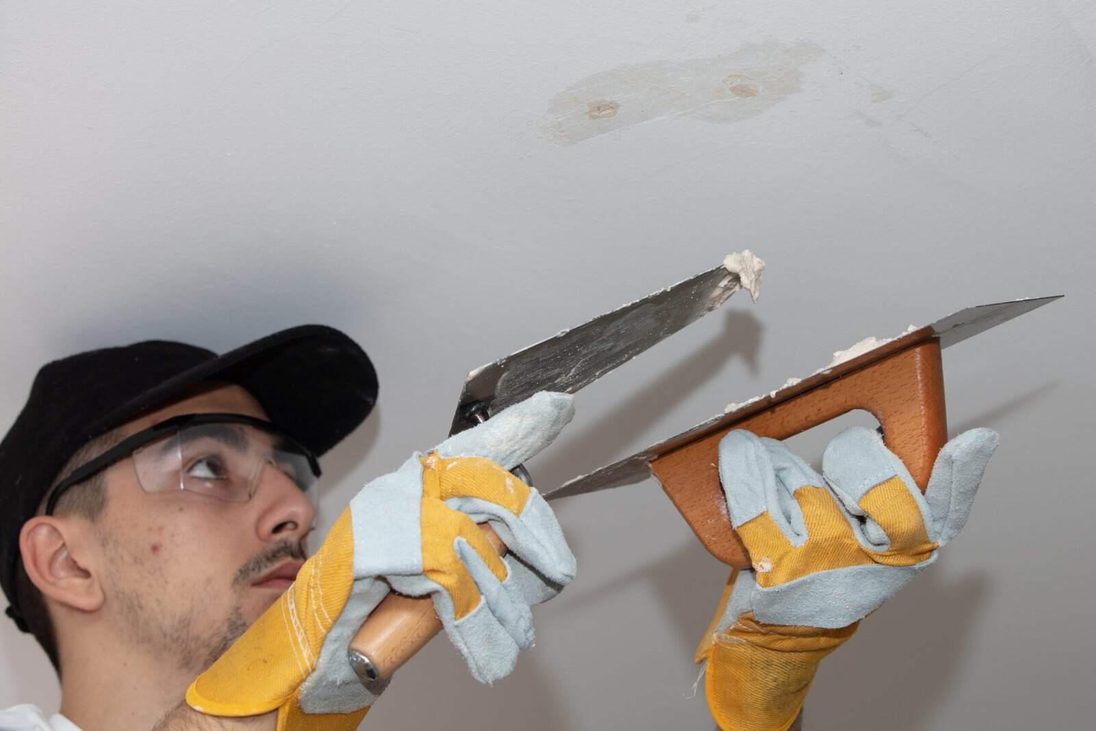 Painter repairing ceiling with putty knife and drywall knife in home interior.