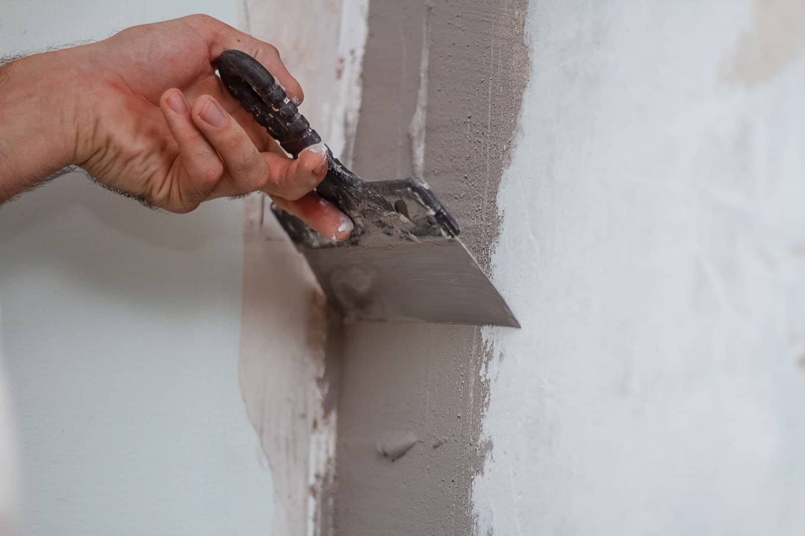 Professional painter applying wall plaster with a trowel for a smooth finish.