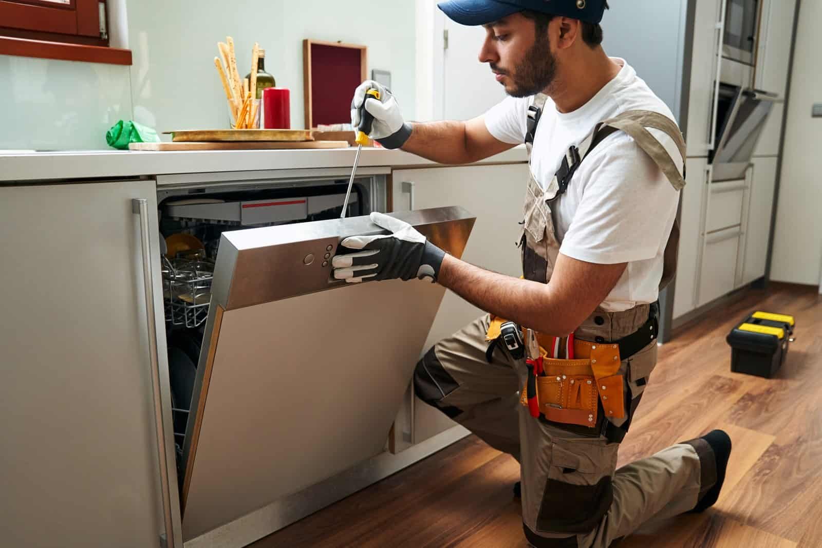 Professional technician repairing dishwasher in modern kitchen.