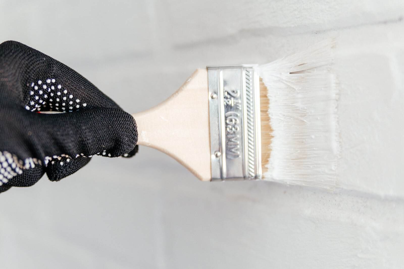 Painter's brush applying white paint to a wall for home improvement.
