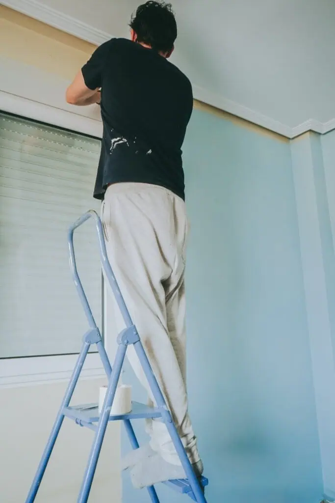 Professional painter applying fresh paint to ceiling in a home interior.
