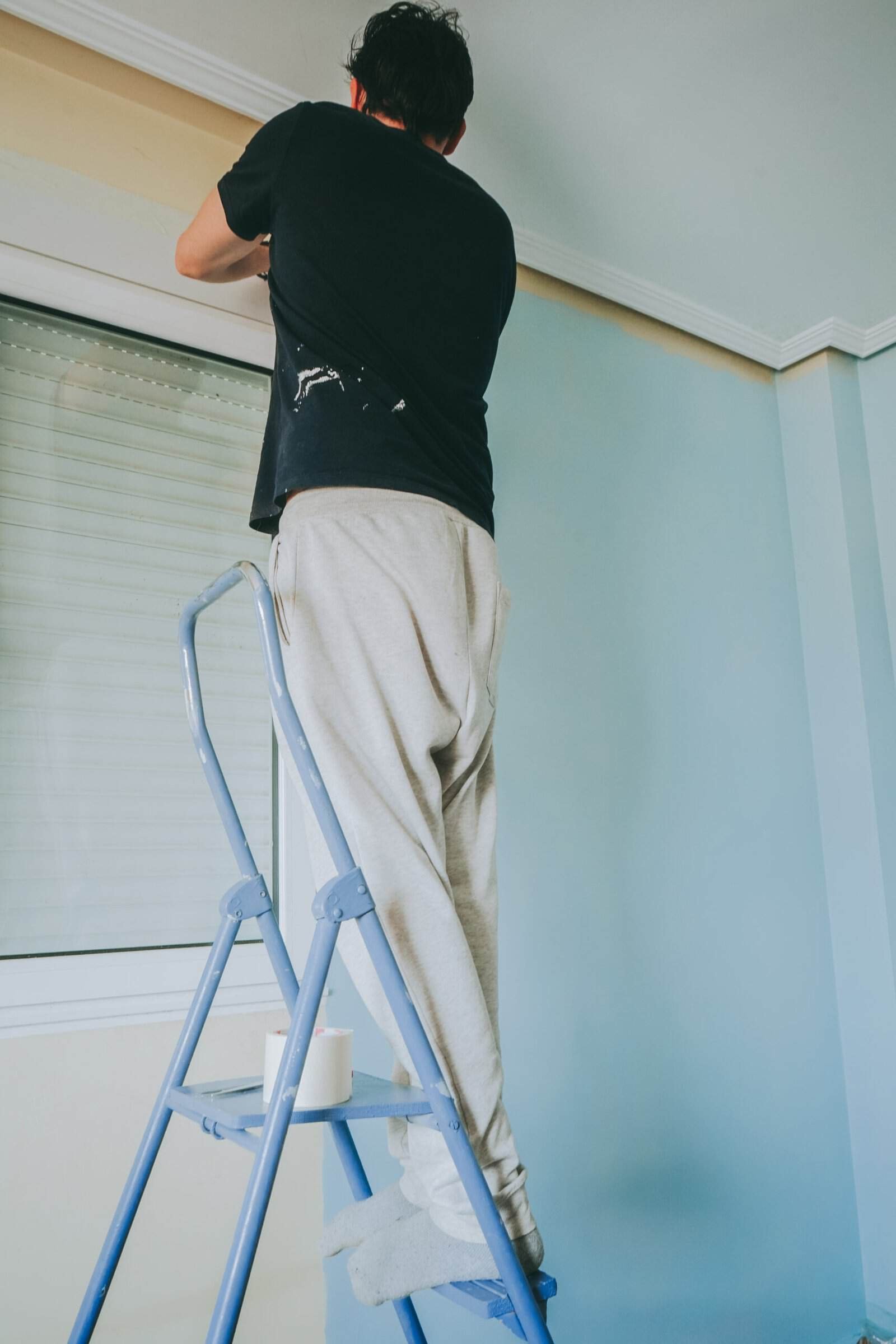 Professional painter applying fresh paint to ceiling in a home interior.