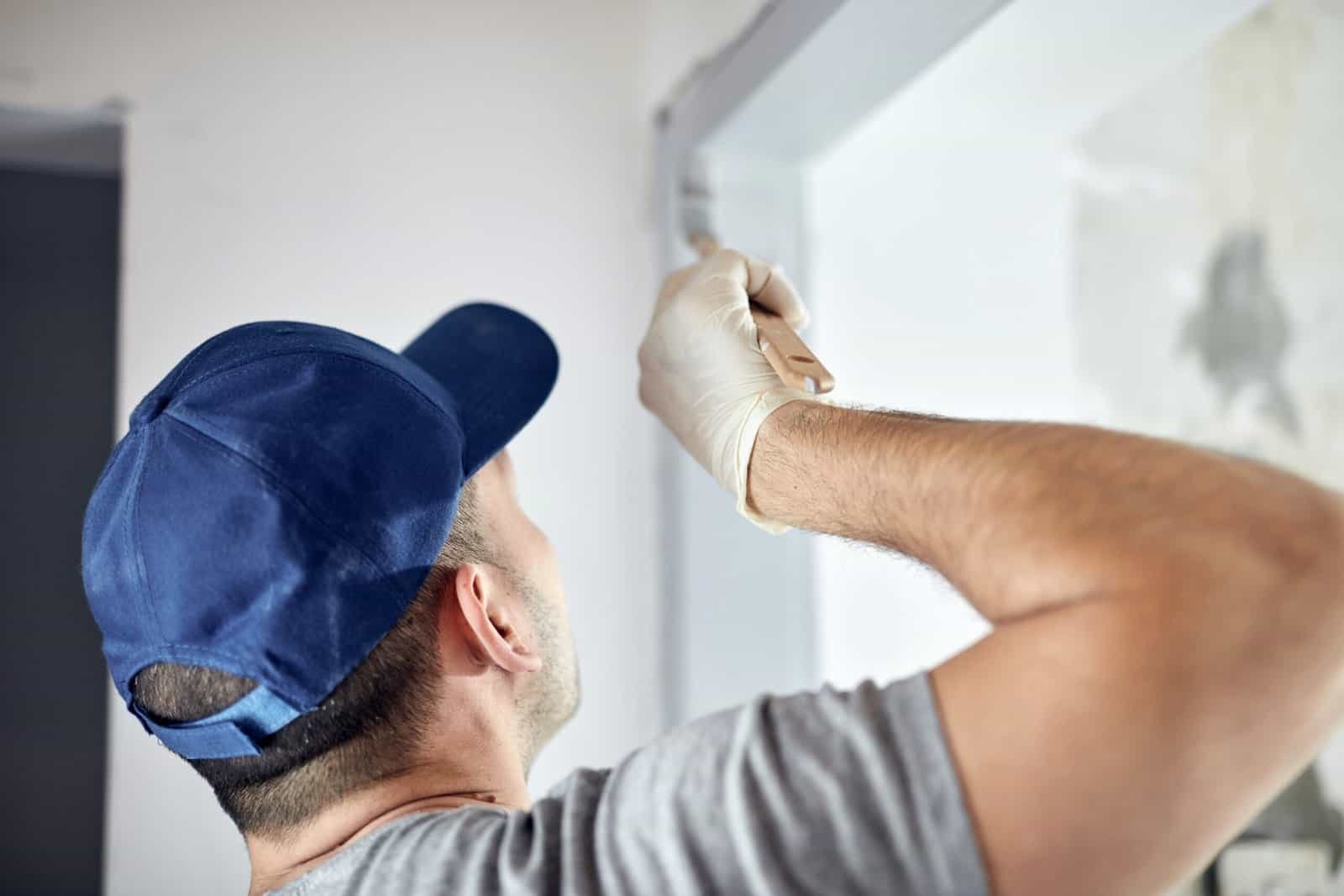 Painter applying paint to interior wall with brush in a home.