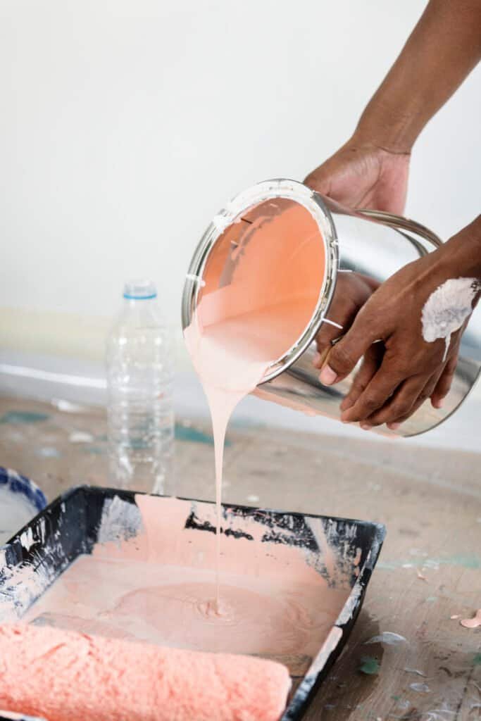 Person pouring peach-colored paint into a tray for painting projects.