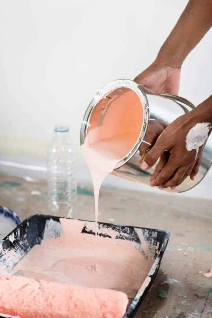 Person pouring peach-colored paint into a tray for painting projects.