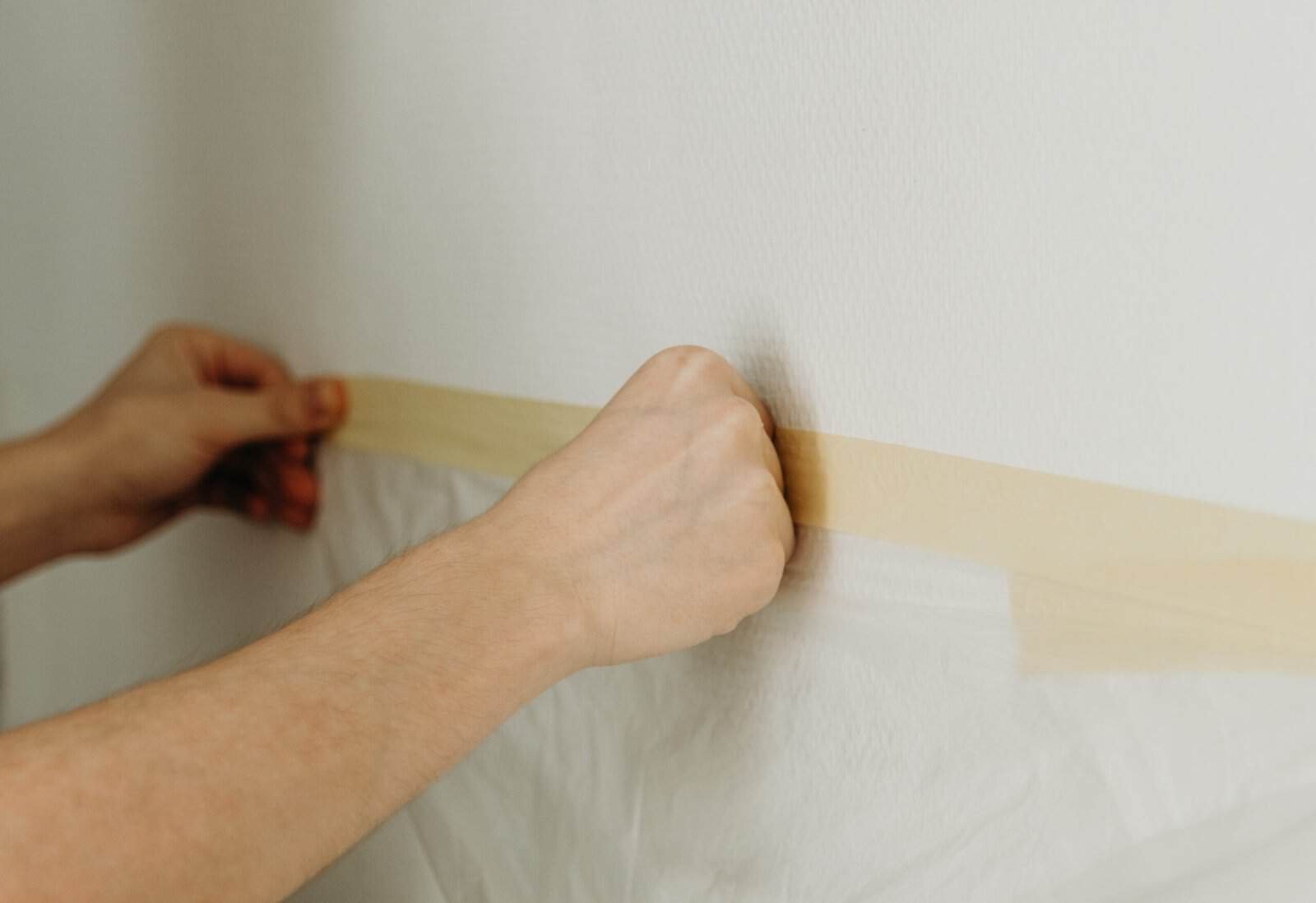 Painter applying painter's tape to wall for painting prep.